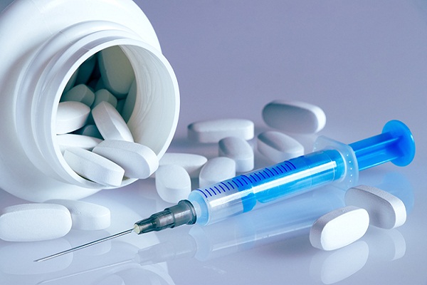 White plastic bottle with medical pills and syringe on a light